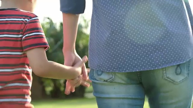 一个男孩在公园里牵着他妈妈的手。视频素材