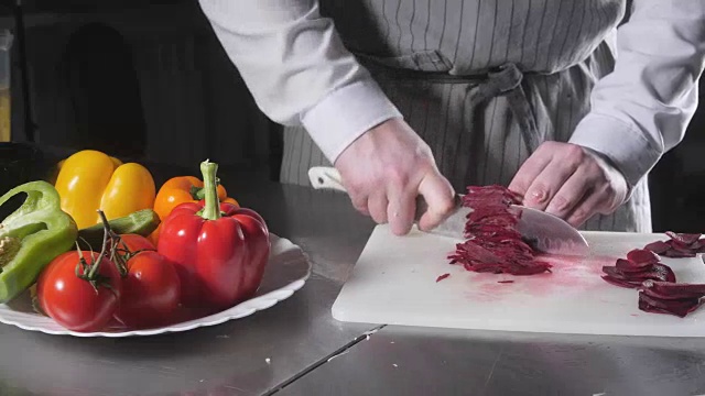 手用刀切新鲜蔬菜的特写。年轻厨师在白色砧板上切甜菜的特写。在餐厅厨房做饭视频素材