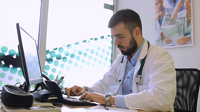一个医生在医院的办公室里用电脑工作。医务人员看着监视器。视频下载