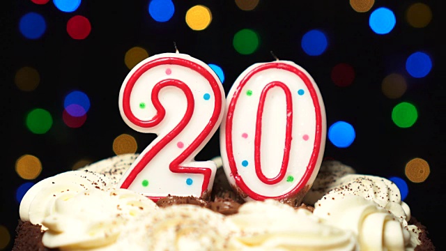 在蛋糕上放20号——二十岁生日蜡烛燃烧——最后吹灭。颜色模糊的背景视频下载