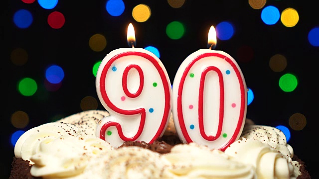 90号放在蛋糕上——90支生日蜡烛燃烧着——最后吹灭。颜色模糊的背景视频下载