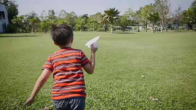 快乐的亚洲男孩在绿色的公园玩纸飞机视频素材