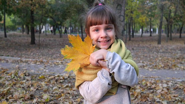 秋天的特写镜头里，可爱的小女孩用黄色的叶子遮住脸，微笑着面对镜头视频素材