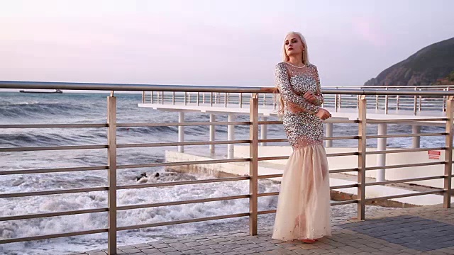 在海边的阳台上，穿着镶着莱茵石的长晚礼服的女孩视频下载