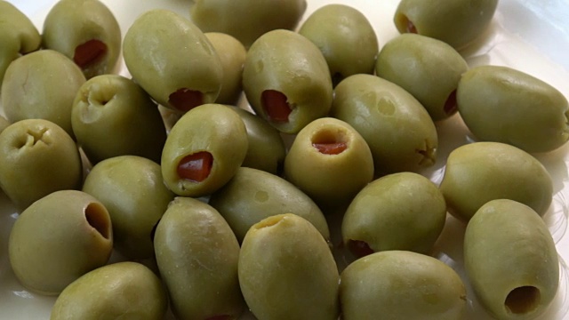 美味的绿橄榄塞满红辣椒在白色的盘子在木制的背景。乡村风格。视频素材