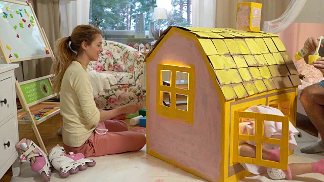 年轻的家庭和孩子一起建造和油漆玩具纸板房子视频素材