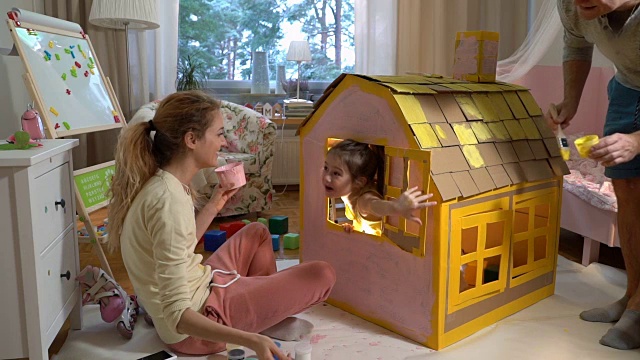 年轻的家庭和孩子一起建造和油漆玩具纸板房子视频下载