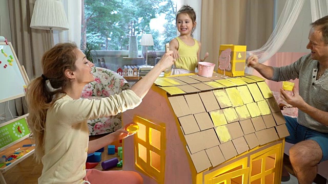 年轻的家庭和孩子一起建造和油漆玩具纸板房子视频素材