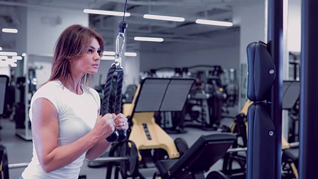 成年妇女在健身房里做三头肌锻炼。健身女孩在健身房做三头肌下推运动视频素材
