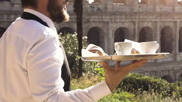 优雅微笑的服务员提供早餐早餐咖啡牛角卡布奇诺在户外尝试在罗马斗牛场前的酒吧餐厅桌子在日落视频下载