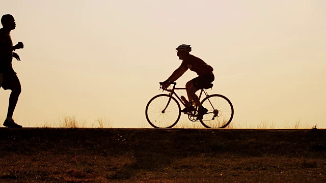 日出时跑步者和骑自行车者的剪影视频下载