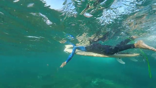 水下慢动作:一个阳光明媚的日子里，职业冲浪运动员在他的冲浪板上划水。视频素材