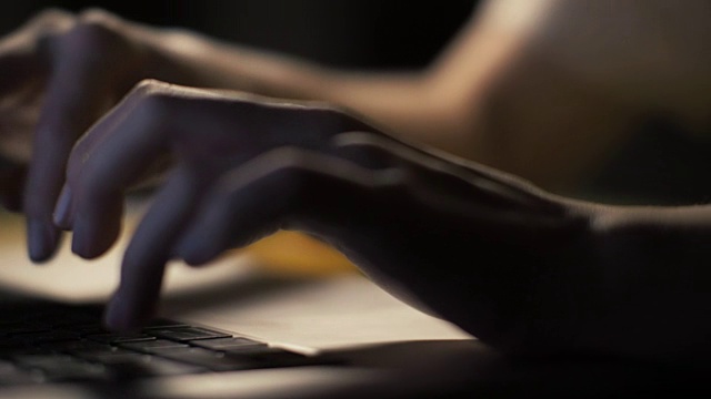 在黑暗的室内，女性的手在现代笔记本电脑的键盘上打字视频素材