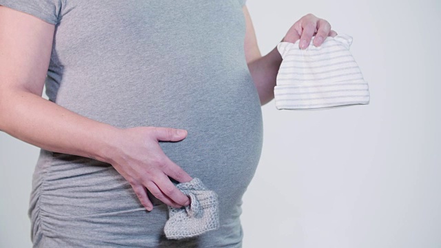 怀孕的母亲抱着婴儿鞋帽子在手上隆起的肚子视频素材