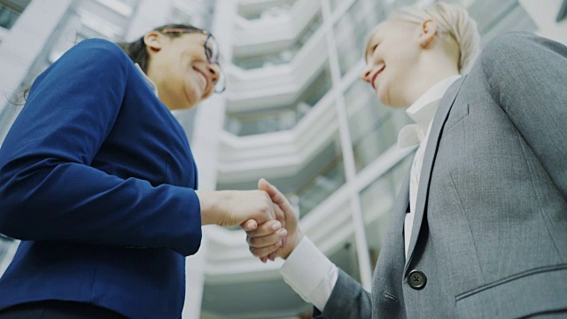 低角度拍摄的女商人与女业务同事在现代办公大楼大厅握手和交谈视频素材