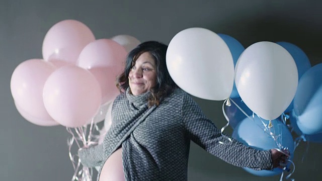 怀孕的妈妈不确定肚子里是男孩还是女孩，用蓝白粉气球象征怀孕视频素材