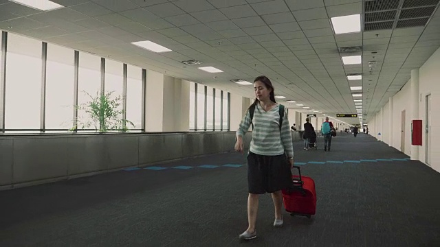 带着红色行李的女旅客走过机场航站楼视频素材