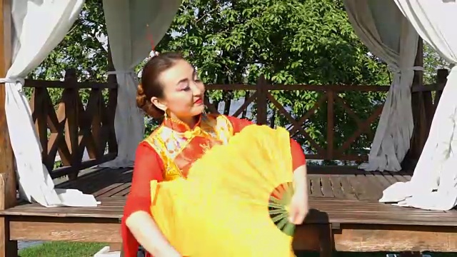 美丽的亚洲女人穿着红色的传统中国服装和两个大的黄色扇子跳舞。视频素材