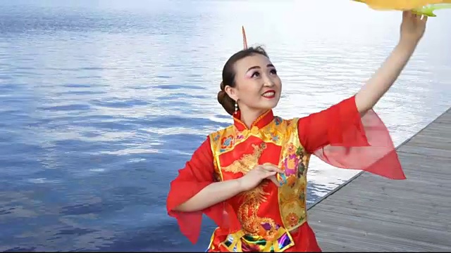 美丽的中国女孩穿着传统的红色中国服装和大的黄色扇子在河边视频素材