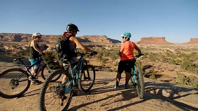 三个冒险的朋友骑着山地车微笑着俯瞰风景优美的沙漠景观。视频素材