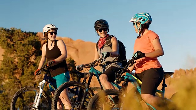 三个骑山地自行车的朋友在摩押沙漠小径上有说有笑。视频素材