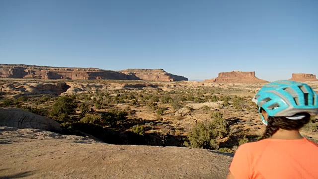 在峡谷地国家公园里，爱冒险的女人骑着山地车指着远处的山丘。视频素材