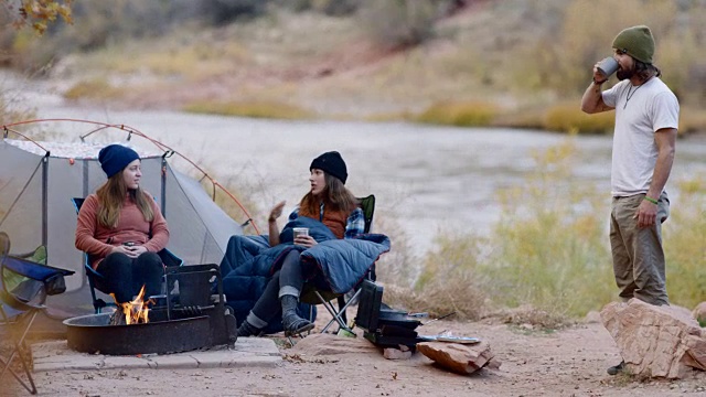 一群朋友在河边的营地旁喝着咖啡聊天。视频素材