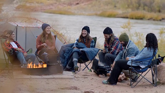 一群朋友在河边露营地的火坑旁欢笑。视频素材