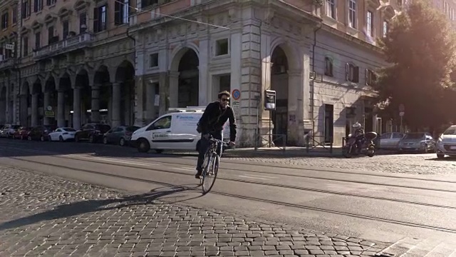 在阳光明媚的日子里，年轻的潮男骑着自行车在罗马市中心一条有树的道路上，戴着墨镜视频素材