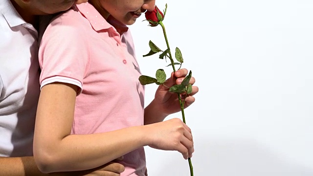 女人很高兴有红玫瑰，在情人节，女人穿粉红色马球衫和男朋友在背后白色孤立的背景。视频素材