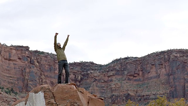在攀登犹他州摩押市的岩石山峰后，一名年轻人挥舞着拳头，欢呼雀跃。视频素材