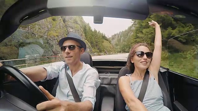4K视频:快乐情侣唱着歌，无顶敞篷车在山路上行驶。视频素材