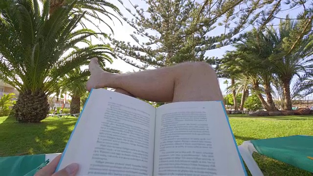 一名男子正在热带花园的日光浴床上看4K慢镜头的书视频素材