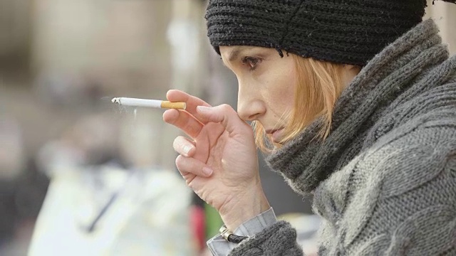 悲伤忧郁的金发女人坐在人行道上抽烟视频下载