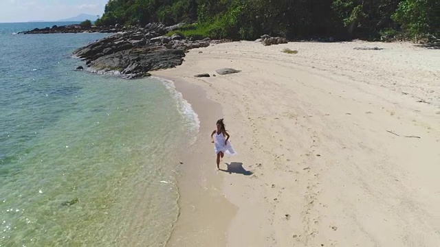一个穿着白色裙子的女孩正沿着海边跑步。视频素材