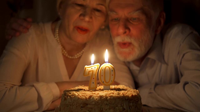 相爱的老夫妇晚上在家用蛋糕庆祝70周年纪念日。吹灭蜡烛视频下载