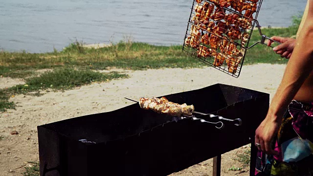 一个男人在准备湖边烧烤。他打开火上的肉视频下载