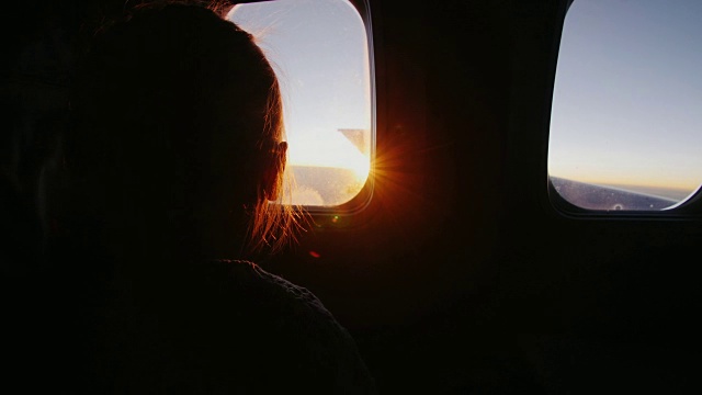 小女孩坐在飞机上，高兴地看着窗外冉冉升起的太阳视频素材