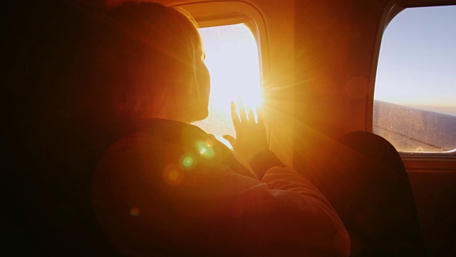 一个女人正从飞机的窗口欣赏日出。她的手触摸着橙色的光线视频素材