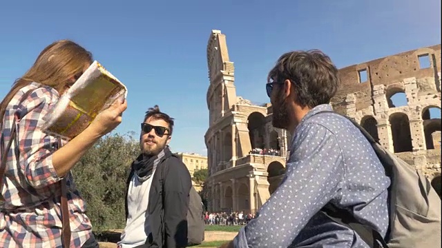 三个年轻的朋友观光客坐在罗马斗牛场前谈论在君士坦丁拱门附近玩的背包太阳镜快乐美丽的女孩长头发视频素材