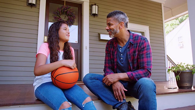 爸爸和女儿在家的门廊上讨论篮球视频素材