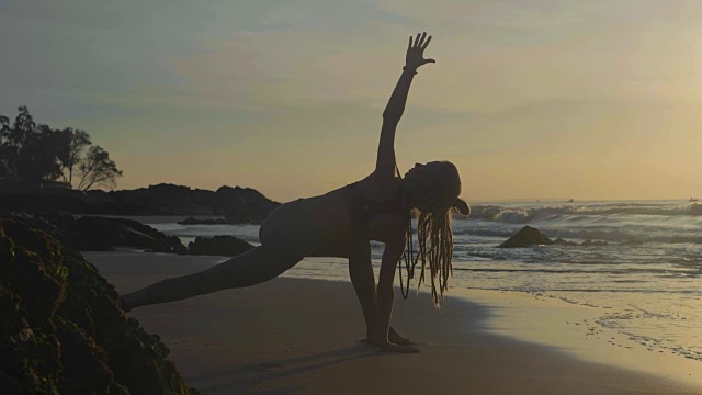 日落时练习剪影瑜伽。一个年轻女人在海滩上做瑜伽运动视频素材