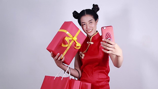 妇女穿着旗袍，用手机与购物袋和礼盒自拍视频下载