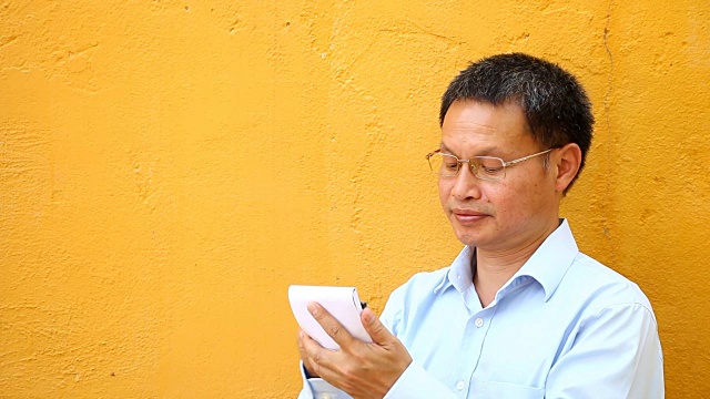 一名泰国男子在写黄色背景的笔记本视频下载