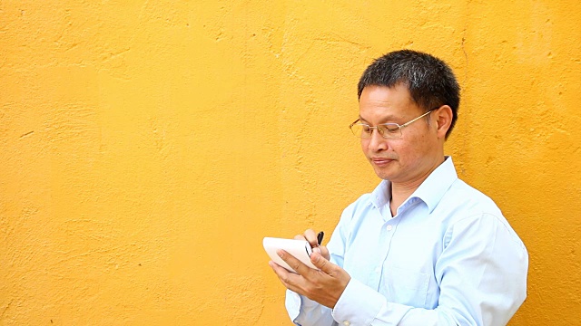 一名泰国男子在写黄色背景的笔记本视频下载