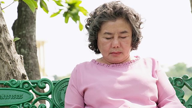 老太太睡着了，瞌睡的奶奶坐在公园的长椅上。视频下载