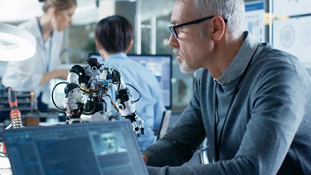 高级机器人工程师操纵语音控制机器人，笔记本电脑屏幕显示软件使用机器学习技术。在机器人研究中心实验室。视频素材