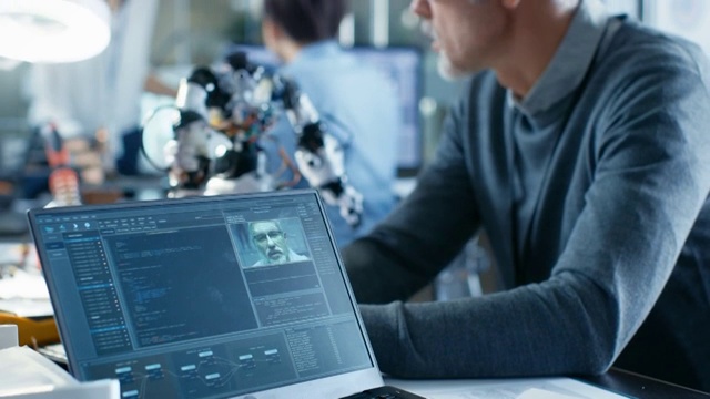 高级机器人工程师操纵语音控制机器人，笔记本电脑屏幕显示软件使用机器学习技术。在机器人研究中心实验室。视频下载