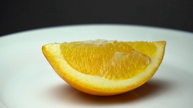 一块新鲜的橘子在白色的盘子上旋转着，上面有水滴。视频素材