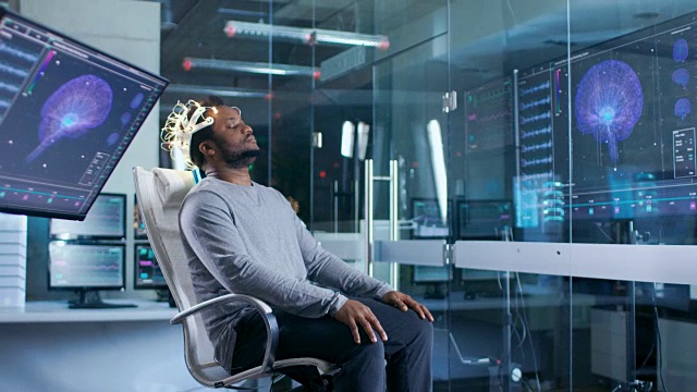 在实验室里，戴着脑电波扫描耳机的人闭着眼睛坐在椅子上。在现代大脑研究/神经研究实验室。监视器显示脑电图阅读和图形大脑模型。视频素材
